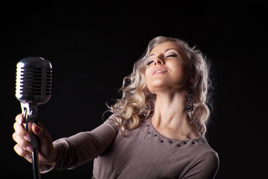 Beautiful blond woman sing in microphone with passion in dark