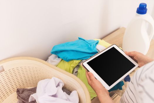 close-up of a woman's hands holding an ipad over clothes, a basin with textiles stands nearby. The concept of reasonable consumption, distribution, processing of textiles. Mockup for design.