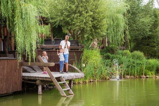 Long shot, dad and son caught a fish. The girl rejoices next to them. Sunny warm summer day. Beautiful greenery around a small lake. The concept of a happy. International Day of Families