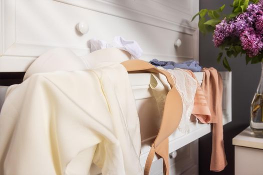 close-up drawers with clothes in a white closet in the apartment, put forward. Lingerie, lace panties, a bra and a tank top in a mess on a shelf. Sun rays in the morning, a bouquet of flowers nearby