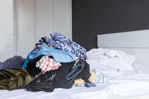 close-up of large pile of colored linen in a mess lies on a white bed in the bedroom, against the background of the closet. Copy paste space for text. The concept of flying lady, Heavy housework woman