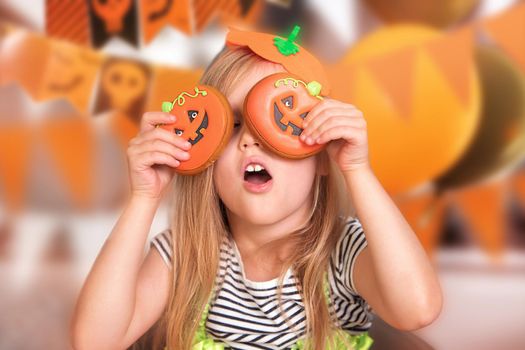 Close-up portrait of a little european girl, a blonde in an orange pumpkin costume for Halloween. The child plays with gingerbread. Children's party at home. Manual production of gingerbread to order.