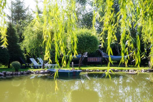 Rural landscape on a sunny summer day. A small lake with wooden boats and a place to relax surrounded by green trees. There are no people around. concept of tranquility meditation and balance