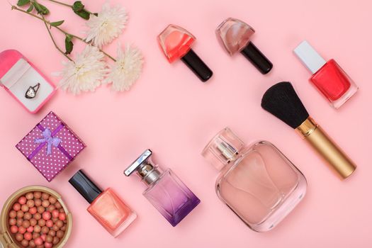 Gift boxes, powder, nail polish, bottle of perfume, lipstick, brush and flowers on a pink background. Women cosmetics. Top view.
