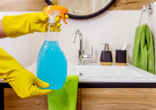 Close-up, female hands in yellow rubber gloves hold a bottle of blue liquid cleaning agent for cleaning the bathroom. Cleaning product mockup, space for logo and label