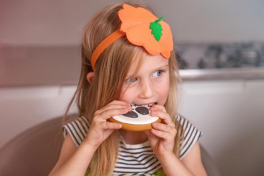 close-up, portrait of a girl in a pumpkin costume for a Halloween party. She's eating sugar-coated gingerbread cookies with a painted face. The concept of a homely cozy holiday, a treat for the family