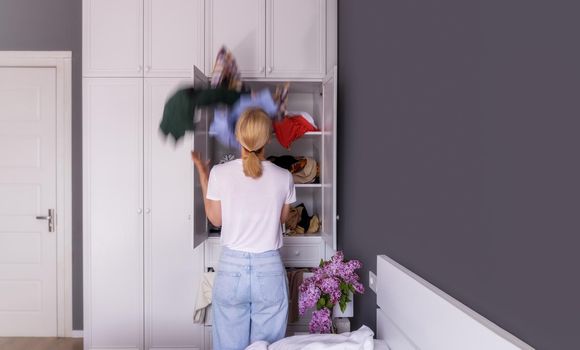 the woman stands with her back and looks into the closet in which there is a big mess, she wants to put things in order. general plan, copy space. The concept of space organization, clutter