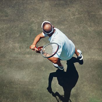 A perfect back swing. High angle shot of a focused middle aged man playing tennis outside on a tennis court during the day