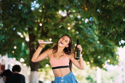 A young woman carries a plate of snacks in one hand and a drink in the other
