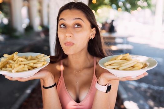 Women hold french fries on white plates. Street cafe