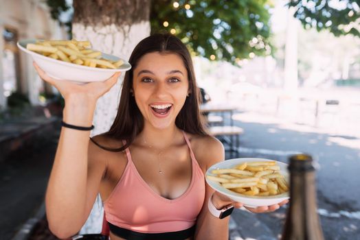 Women hold french fries on white plates. Street cafe