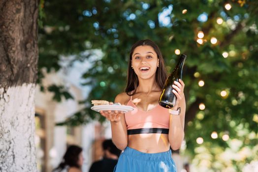 A young woman carries a plate of snacks in one hand and a drink in the other