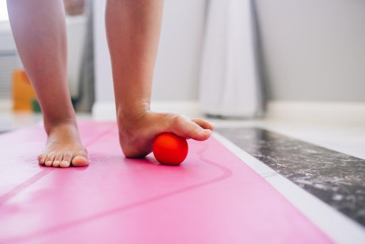 Woman massages the foot with a ball. The ball will apply pressure to the painful spot and raise the procedure