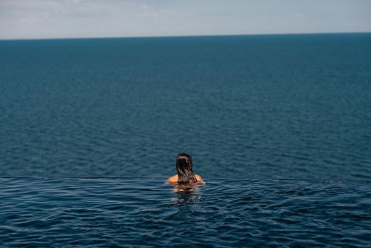 Happy woman in swimsuit swimming in infinity pool at luxury hotel against seafront. Relaxing, summer, travel, holiday, vacation and weekend concept