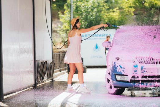 Brunette with long hair from a high-pressure hose applies a cleaner on the car at a car wash