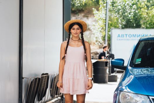 Beautiful young woman in a short dress with tails and a hat at the car wash