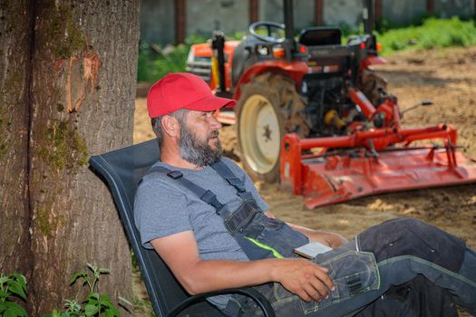 Tractor driver rests in the shade of a tree after plowing the land. Agricultural work on the site.
