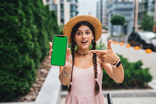 young woman showing smartphone with green screen for replacement
