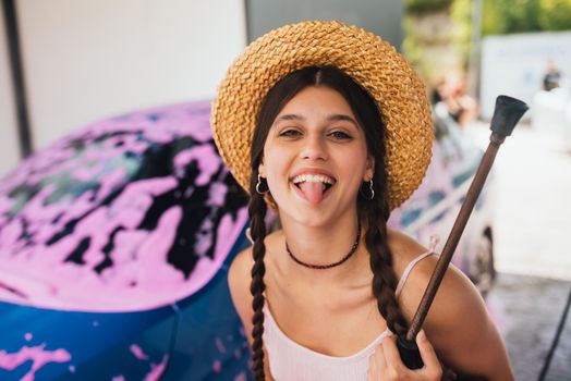 Young woman with high pressure hose stands by car covered in pink foam