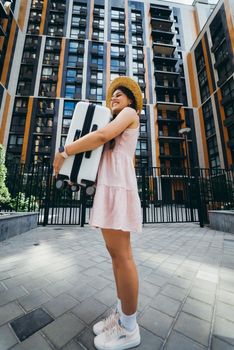 A young beautiful woman holds a suitcase in her hands in front of a modern house