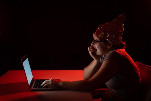Paranoid caucasian woman typing on a computer wearing a tinfoil cap. Conspiracy theory