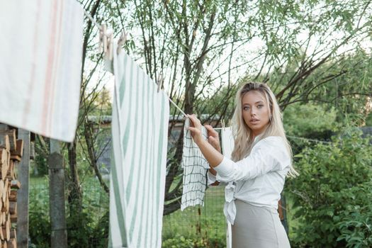 Laundry day. A woman hangs linen and towels on a tree in the courtyard of a village house. Summer cottage concept.