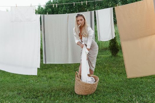 Laundry day. A woman hangs linen and towels on a tree in the courtyard of a village house. Summer cottage concept.