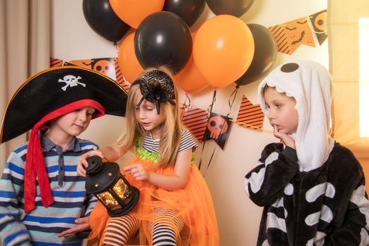 Close-up, three children celebrate Halloween at home. A family in carnival costumes, a skeleton, a pirate and a witch light a small lantern. One sad boy aside, he was not taken to the game along