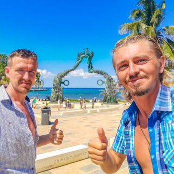 Tourists travelers and tour guides at ancient architecture of the Portal Maya in the Fundadores park with blue sky and turquoise seascape and beach panorama in Playa del Carmen Quintana Roo Mexico.