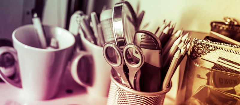 Writing instruments in glasses on a shelf.