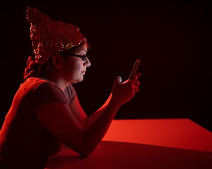 Paranoid caucasian woman using smartphone wearing tinfoil hat. Conspiracy theory