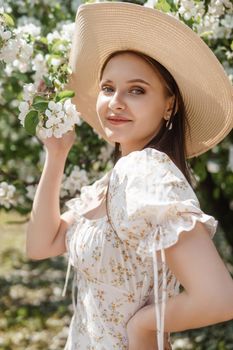 An attractive long-haired woman walks in the spring in the park of blooming apple trees. Spring portrait of a woman