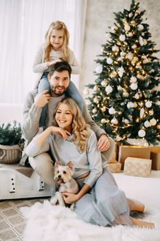 Happy family: mom, dad and pet. Family in a bright New Year's interior with a Christmas tree.