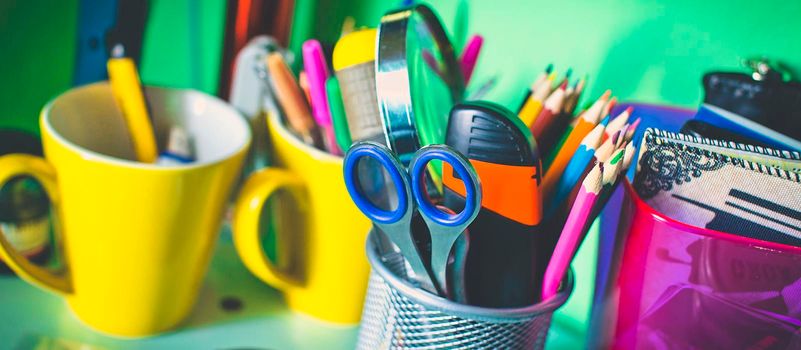 Writing instruments in glasses on a shelf.