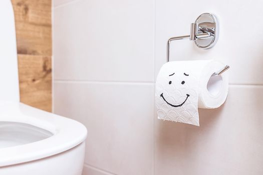 Close-up of a toilet paper roll with a funny smiley face hanging on the wall in the bathroom. The concept of good health, clean bathroom, happy life