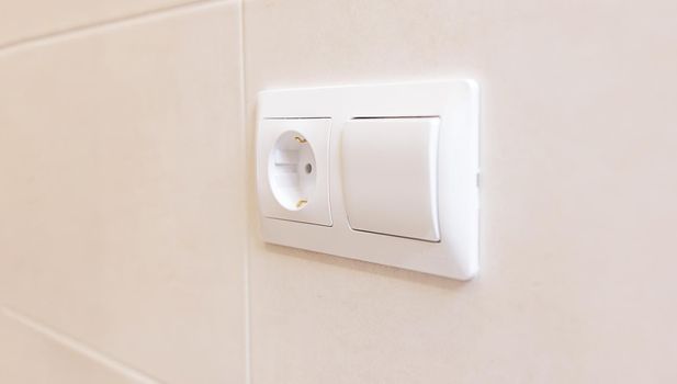 close-up of an electric socket and a light switch on a white ceramic tile wall. White copy paste space for your design. Modern European interior