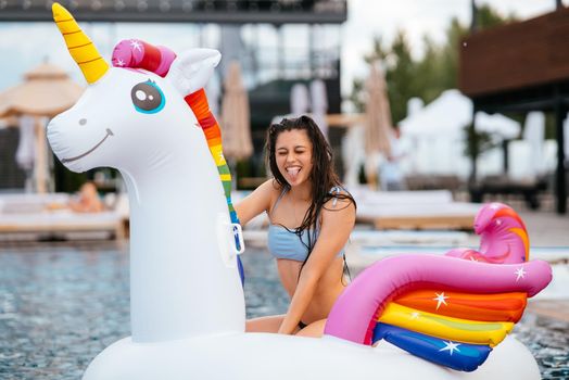 Woman in bikini in inflatable unicorn toy mattress float in pool. Girl relaxing sunbathing enjoying travel holidays at resort pool