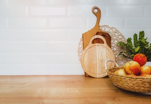 Kitchen utensils on the tabletop, culinary background, wooden boards and red fresh apples in a basket. home cooking concept. Large, empty piece of white wall, copy paste
