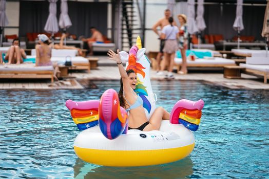 Woman in bikini in inflatable unicorn toy mattress float in pool. Girl relaxing sunbathing enjoying travel holidays at resort pool