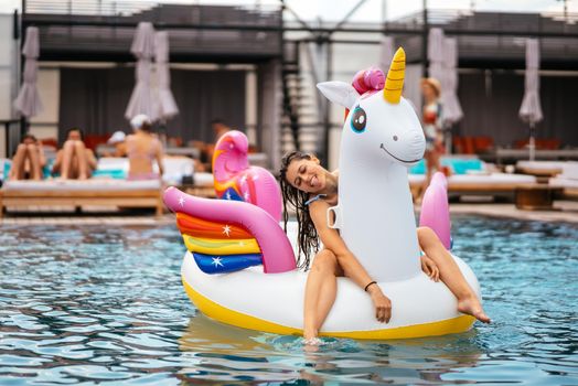Woman in bikini in inflatable unicorn toy mattress float in pool. Girl relaxing sunbathing enjoying travel holidays at resort pool
