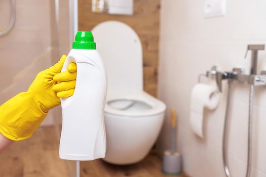 White bottle mockup for cleaning. The concept of hygiene, cleaning the house or public place, close-up female hands in protective yellow gloves with liquid detergent to disinfect toilet and bathroom