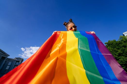 A young woman develops a rainbow flag against the sky in support of the LGBT community