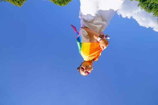 A young woman develops a rainbow flag against the sky in support of the LGBT community
