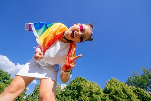 A young woman develops a rainbow flag against the sky in support of the LGBT community