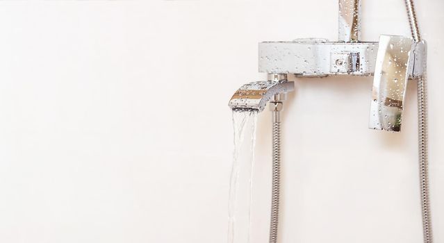 Close-up, plumbing equipment. Chrome plated water faucet hangs from the heart on a white wall, isolated object, copy space. Water flows from the faucet in a strong stream.