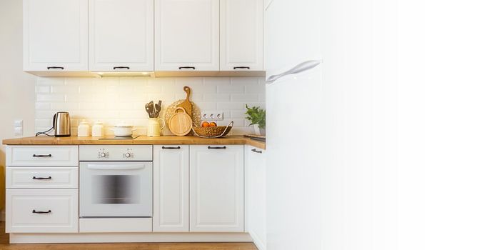 Big banner with white empty space, copy paste. Image of a modern, versatile, illuminated fitted kitchen. There is some equipment and homemade flowers on a wooden table top.