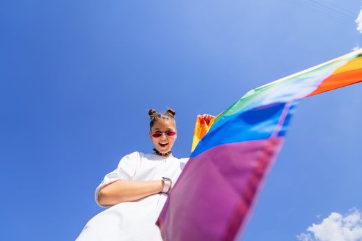 A young woman develops a rainbow flag against the sky in support of the LGBT community