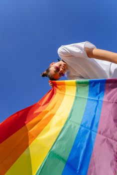 A young woman develops a rainbow flag against the sky in support of the LGBT community