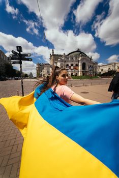 A young woman carries the flag of Ukraine fluttering behind her in the street