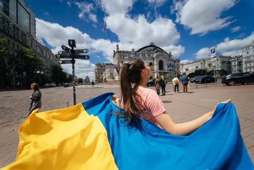 A young woman carries the flag of Ukraine fluttering behind her in the street